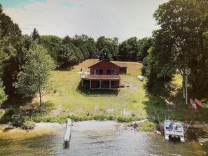 Uma casa de dois andares com uma varanda grande, rodeada por um gramado e árvores.