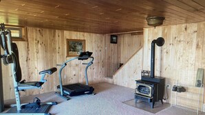 Una habitación de madera con una caminadora, una bicicleta estática y un estufa de leña.