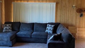 Una habitación con sofá modular, techo de madera y ventana con persianas.