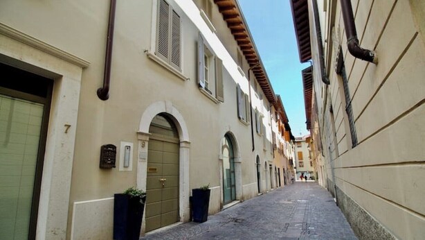 Une ruelle étroite pavée, bordée d’immeubles aux portes et fenêtres en arc de cercle, une grille métallique au sol et un ciel dégagé au-dessus.