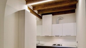 Une cuisine avec des meubles blancs, un sol carrelé et un plafond en bois.