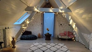 A cozy attic room with a sloped ceiling, a skylight, a patterned rug, a sofa, a bean bag, and string lights. - Zennon II - Feel Good (Geraardsbergen)