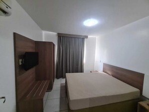 A hotel room with a bed, a TV mounted on the wall, a bench, and a window with curtains.