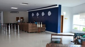 Un área de recepción con un escritorio de madera, una pared azul con relojes y una zona de estar con un sofá y un banco.