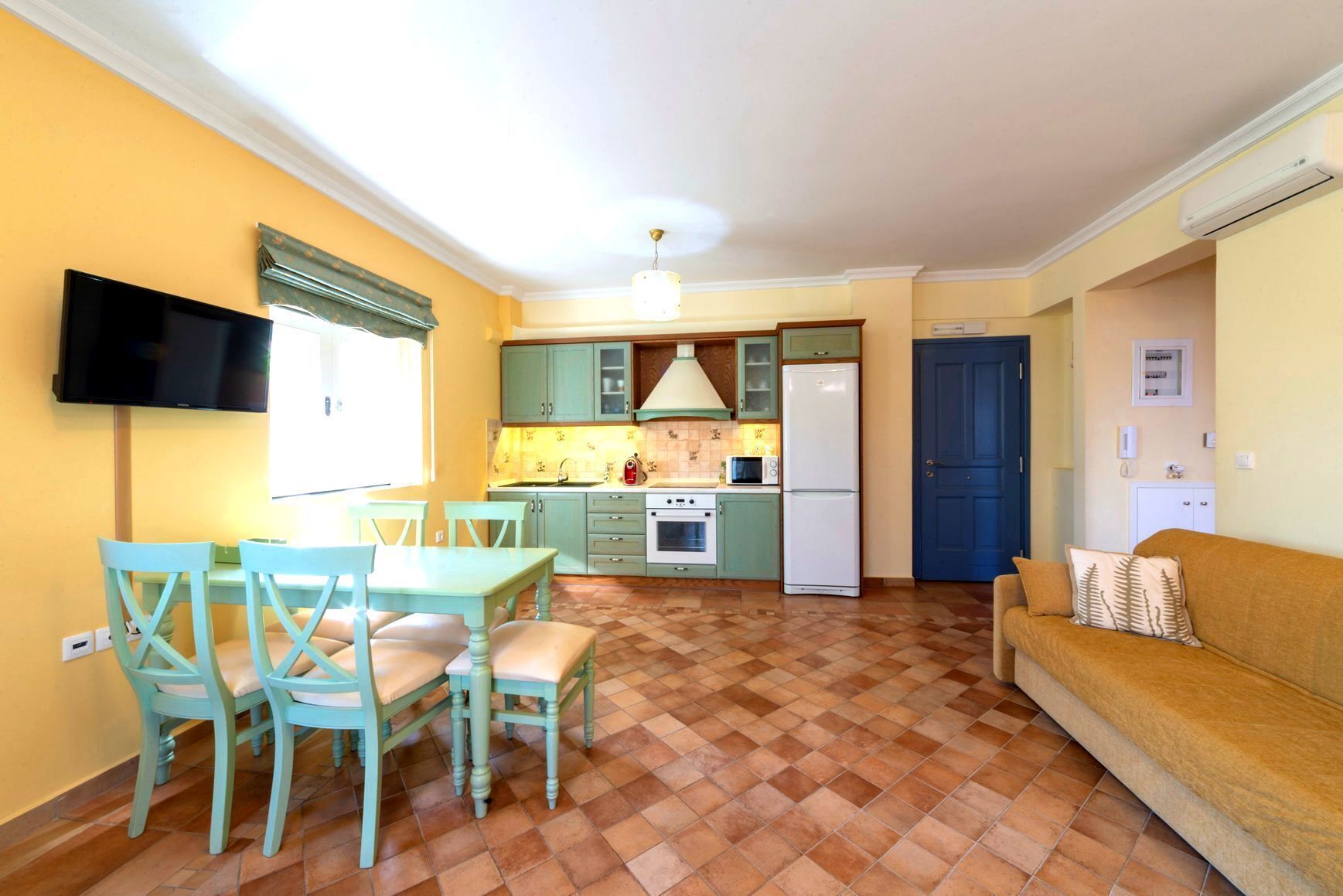 Una cocina compacta con comedor, un televisor de pantalla plana y una puerta azul.