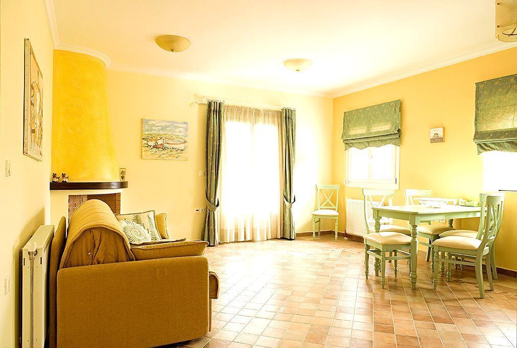 Una sala de estar con sofá, una mesa de comedor con sillas, chimenea y ventana con cortinas.