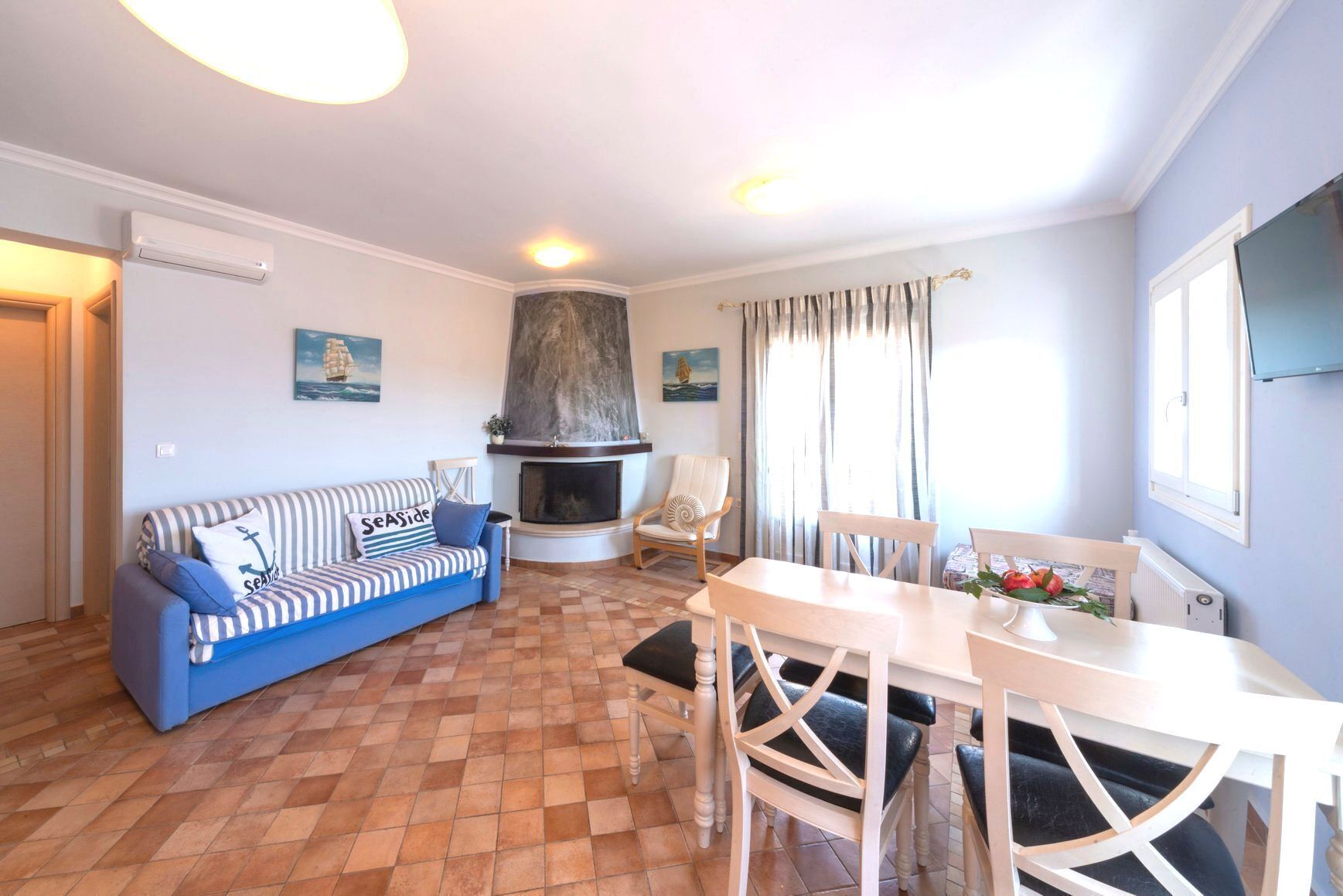 Una sala de estar con sofá, chimenea, mesa de comedor con sillas y televisor montado en la pared.