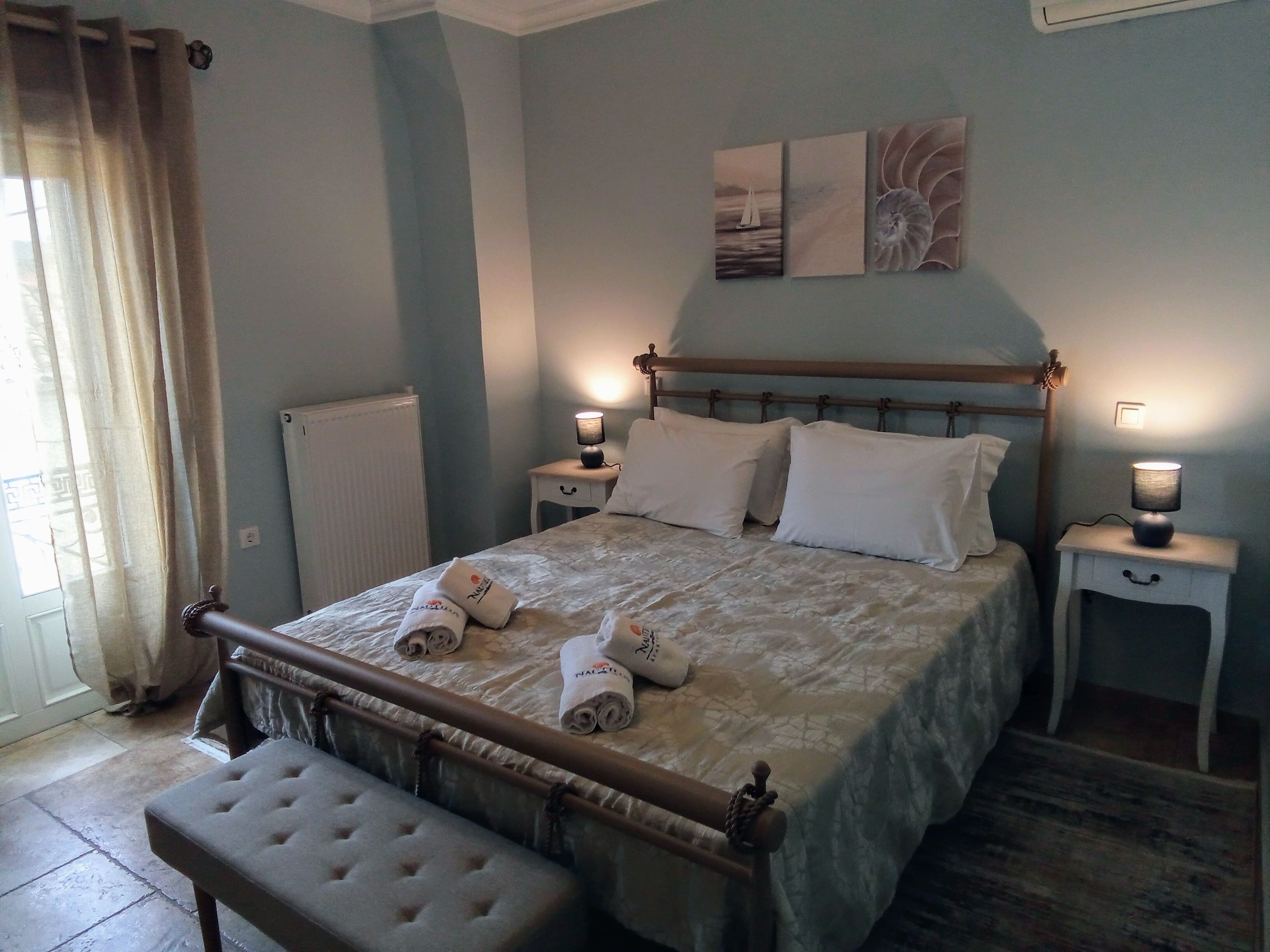 A neatly made bed with white linens and rolled towels, a wooden headboard, bedside tables with lamps, and artwork on the wall.