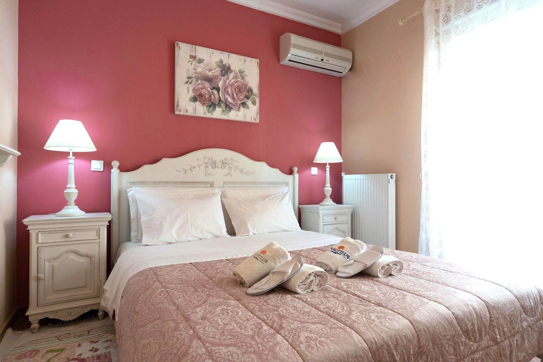 Un lit bien fait, recouvert d’une couvre-lit à motifs roses, avec deux lampes de chevet et une œuvre d’art florale accrochée au-dessus du lit.