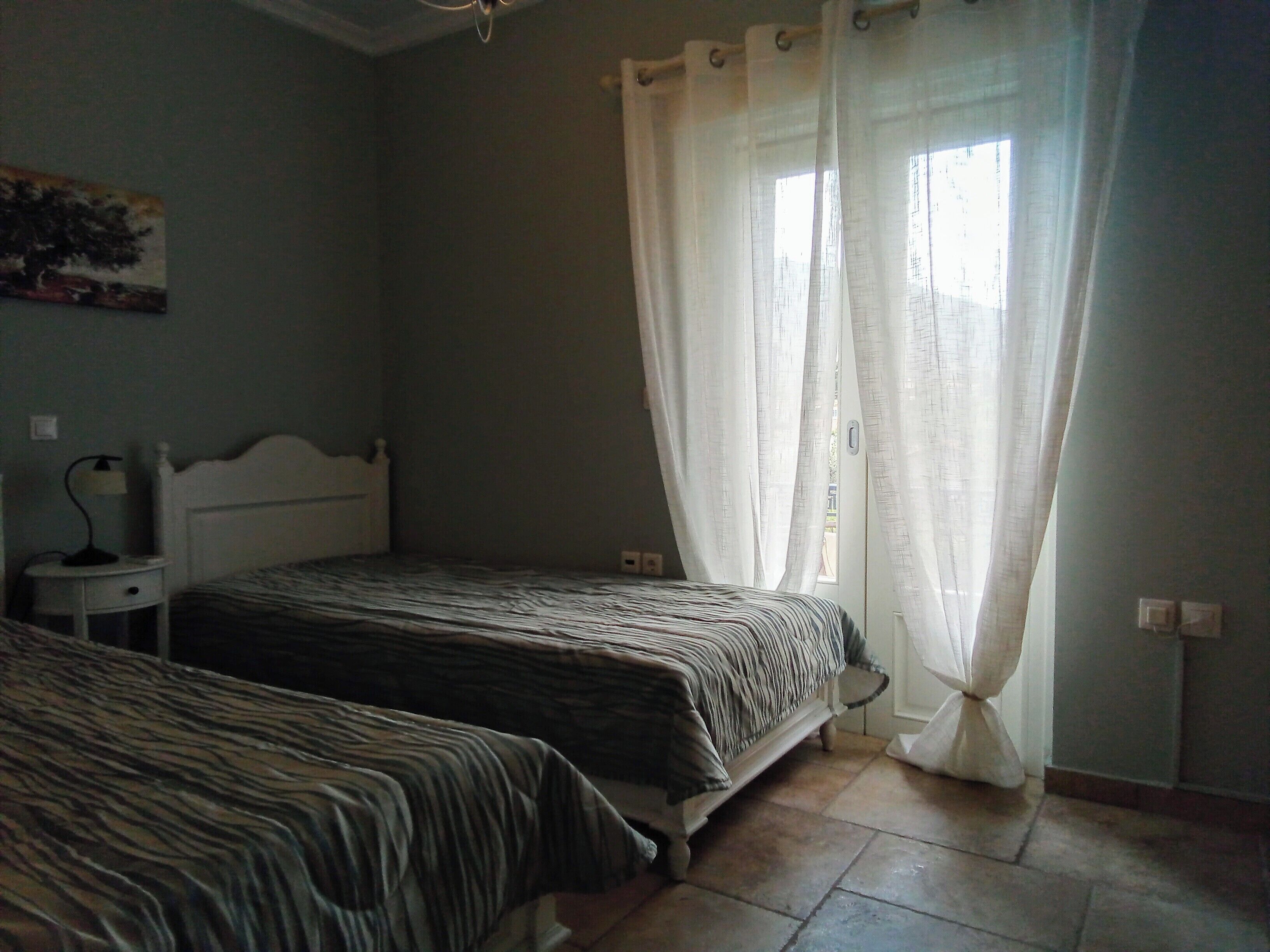 Une chambre avec deux lits, une table de chevet, une lampe et une fenêtre avec des rideaux.