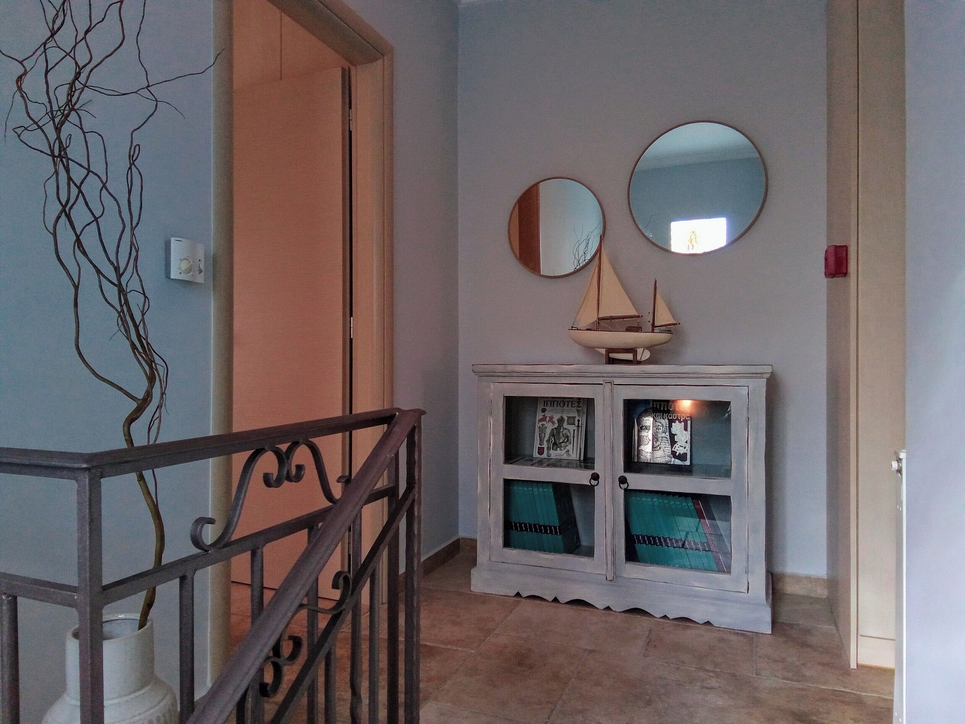 Un pasillo con una escalera, un mueble con puertas de cristal y dos espejos redondos en la pared.