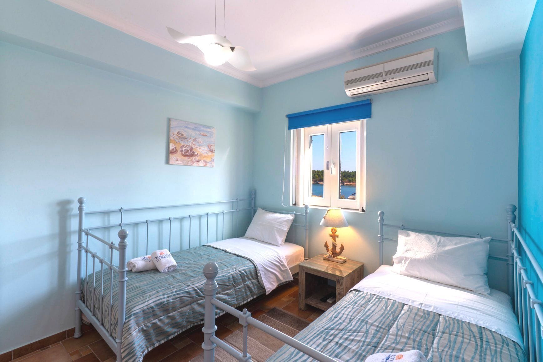 A bedroom with two beds, a window with a view, an air conditioner, and a ceiling fan.