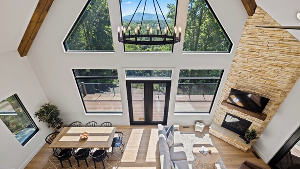 A spacious living area with a high ceiling, large windows, a fireplace, and a dining area with a table and chairs. - BRAND NEW 4BR 4 BATH & BUNK ROOM MODERN MOUNTAIN LODGE WITH BEAUTIFUL VIEWS (Townsend)