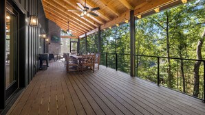 A wooden deck with a table and chairs, a ceiling fan, and a view of trees. - BRAND NEW 4BR 4 BATH & BUNK ROOM MODERN MOUNTAIN LODGE WITH BEAUTIFUL VIEWS (Townsend)