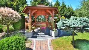 A wooden gazebo with a table and chairs, surrounded by potted plants and trees. - Holiday apartment, 3 bedrooms, garden, Słowino (Slowino)