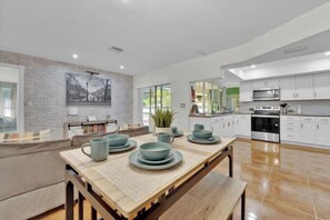 Enjoy meals in the kitchen with stainless steel appliances and a large island, adjacent to a dining area with a wooden table and blue tableware.