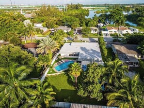 Surrounded by lush greenery and palm trees, this residential area features a swimming pool and a mix of single and two-story houses with flat roofs.