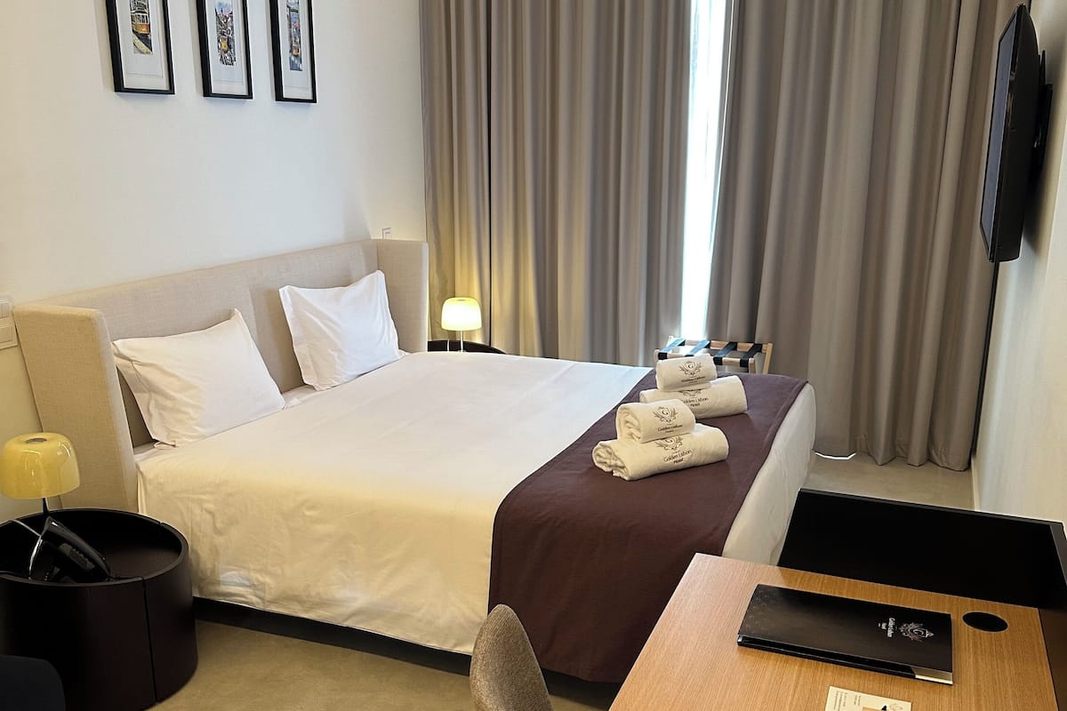 A hotel room with a bed, a desk, a chair, a lamp, and a TV.