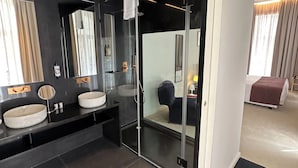 A modern bathroom with a dark theme, featuring two sinks, a large mirror, and a glass shower enclosure. - Golden Lisbon Hotel (Lisbon)