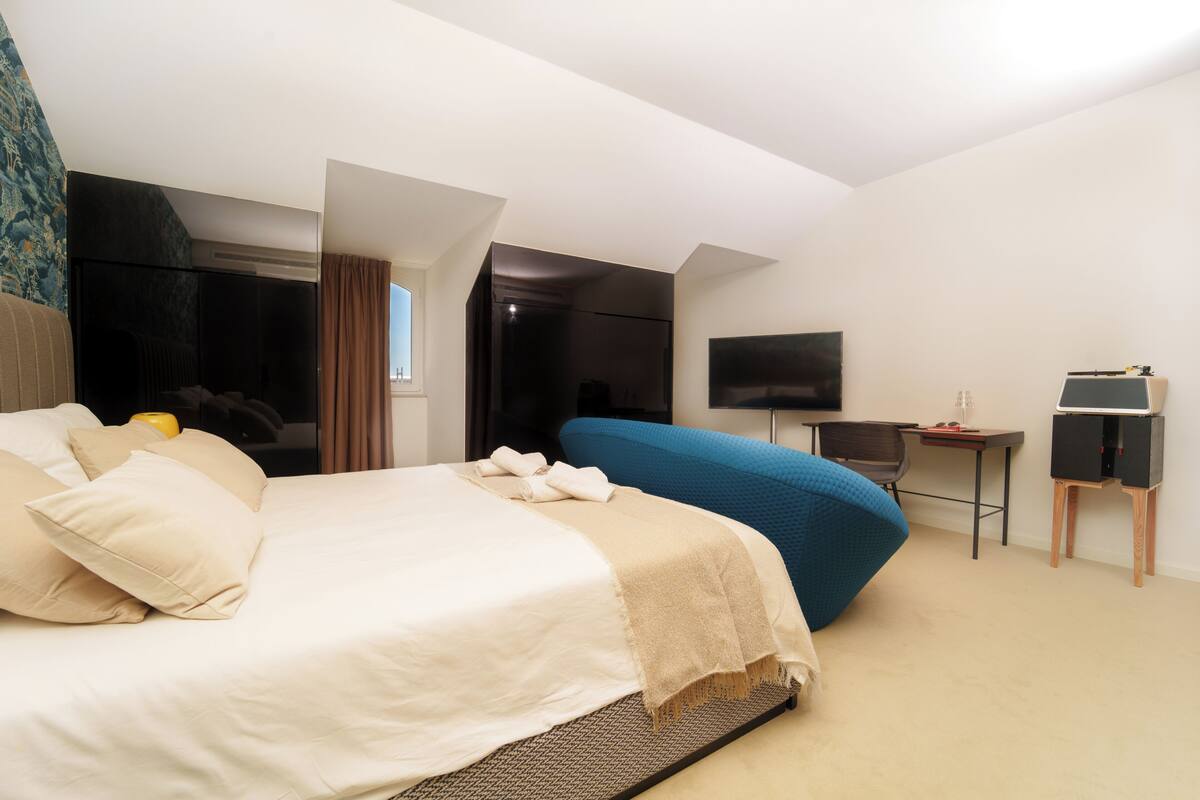 A modern hotel room with a large bed, a desk, a flat-screen TV, and a seating area.