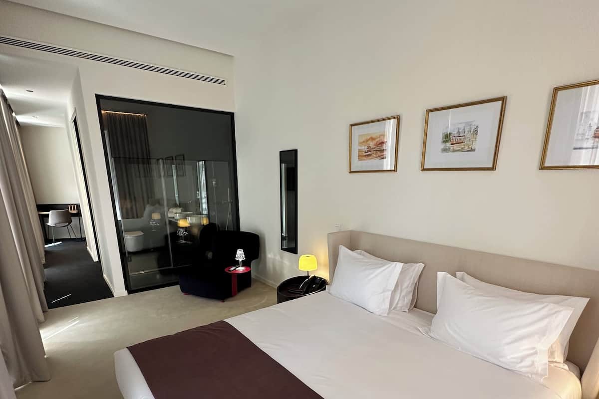 A hotel room with a large bed, a desk with a chair, a mirror, and three framed pictures on the wall.