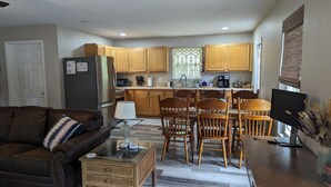 Una cocina moderna con armarios de madera, un refrigerador, una cafetera y un comedor con sillas de madera y una mesa de vidrio.