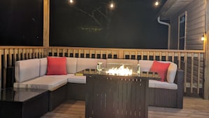 Un área de estar al aire libre con una chimenea, una terraza de madera y luces colgantes.