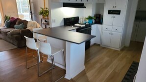 Ett modernt kök med vita skåp, en köksö och barstolar.