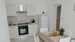 A modern kitchen with white cabinets, a stove, oven, and a dining area with a table and chairs. - La Casa di Katia (Canicatti)