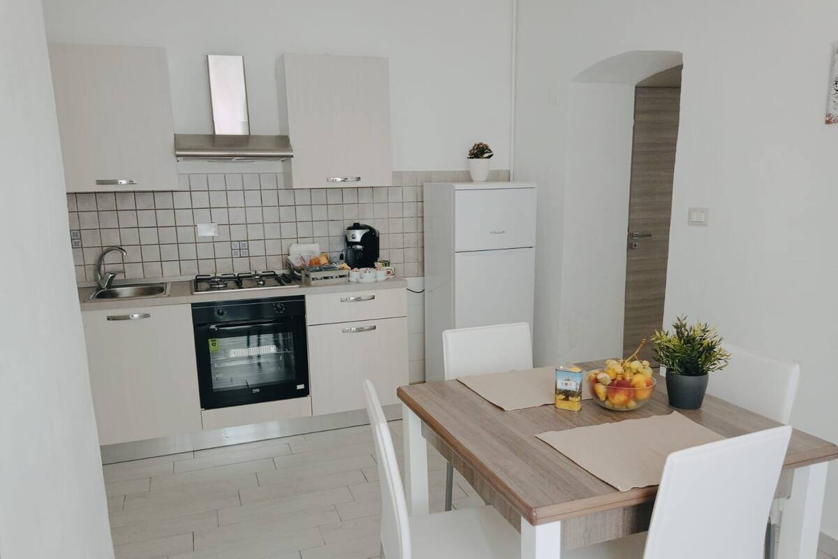 Una cocina moderna con armarios blancos, estufa, horno y un comedor con mesa y sillas.