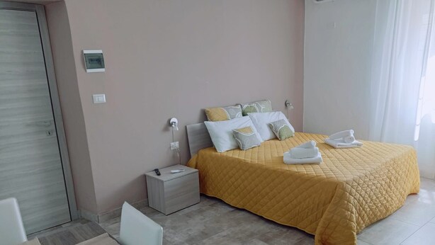 A neatly arranged bedroom with a bed, bedside table, and a small seating area. - La Casa di Katia (Canicatti)