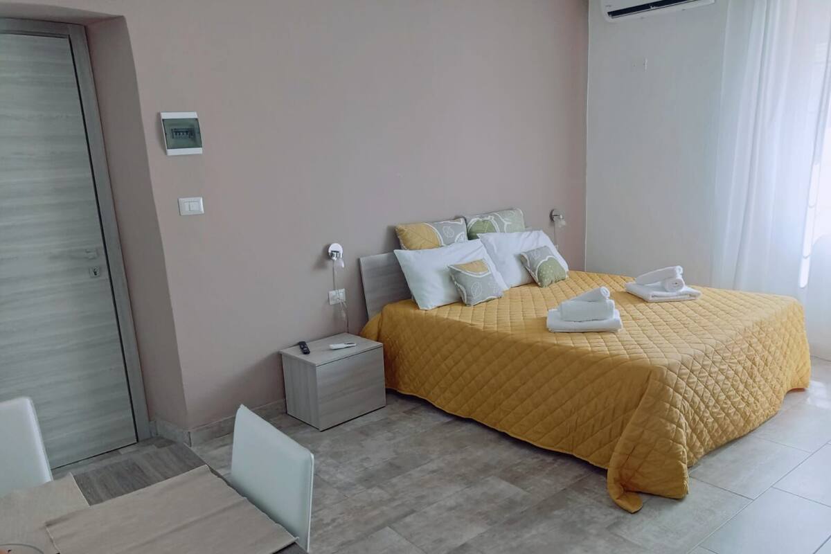 Un dormitorio ordenado con cama, mesita de noche y una pequeña zona de estar.