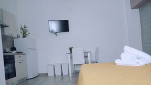 A compact hotel room with a bed, a desk, a chair, a television mounted on the wall, and a small kitchen area with a refrigerator and a microwave. - La Casa di Katia (Canicatti)