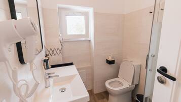 A bathroom with a white sink, a hairdryer, a toilet, and a small window.