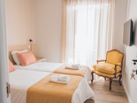 Habitación de hotel con dos camas, una silla y un televisor en la pared.
