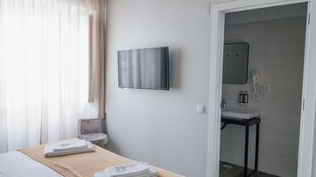 Habitación de hotel con cama, televisor en la pared, baño con lavabo y espejo, y una mesita con toallas.