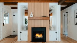 Un intérieur moderne agrémenté d’une cheminée, de poutres en bois et de meubles blancs.