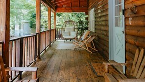 Une cabane en bois avec une véranda, une porte blanche et un banc.