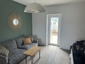 Una sala de estar moderna con un sofá gris, una mesa de centro de madera, una lámpara colgante y un espejo grande en la pared.