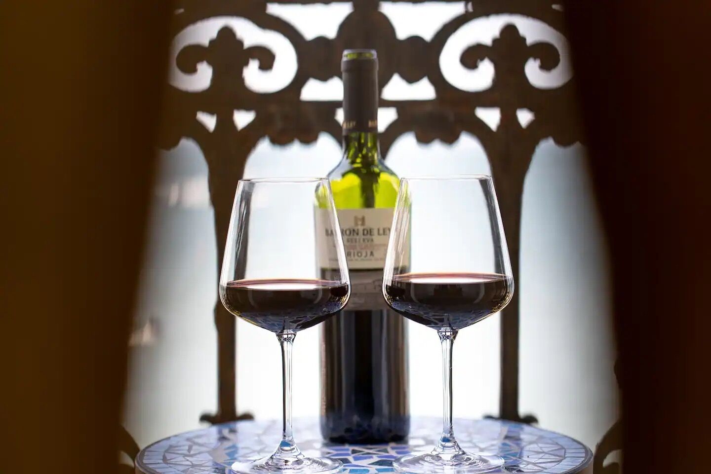 A bottle of wine and two glasses on a table with a decorative metal backdrop.