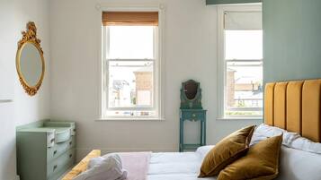 A bedroom with a bed, a dresser, a vanity with a mirror, and two windows with blinds.
