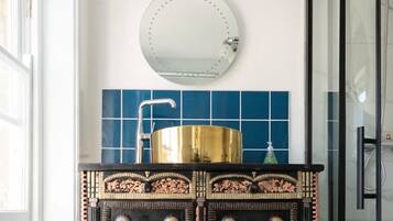 Un baño con un espejo redondo, un lavamanos dorado y azulejos azules.