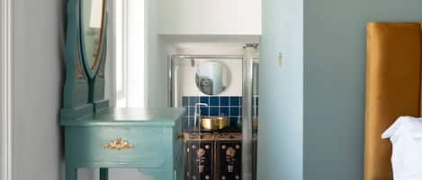 Una habitación con un tocador color turquesa, una cama con cabecera blanca y un baño visible a través de una puerta abierta.