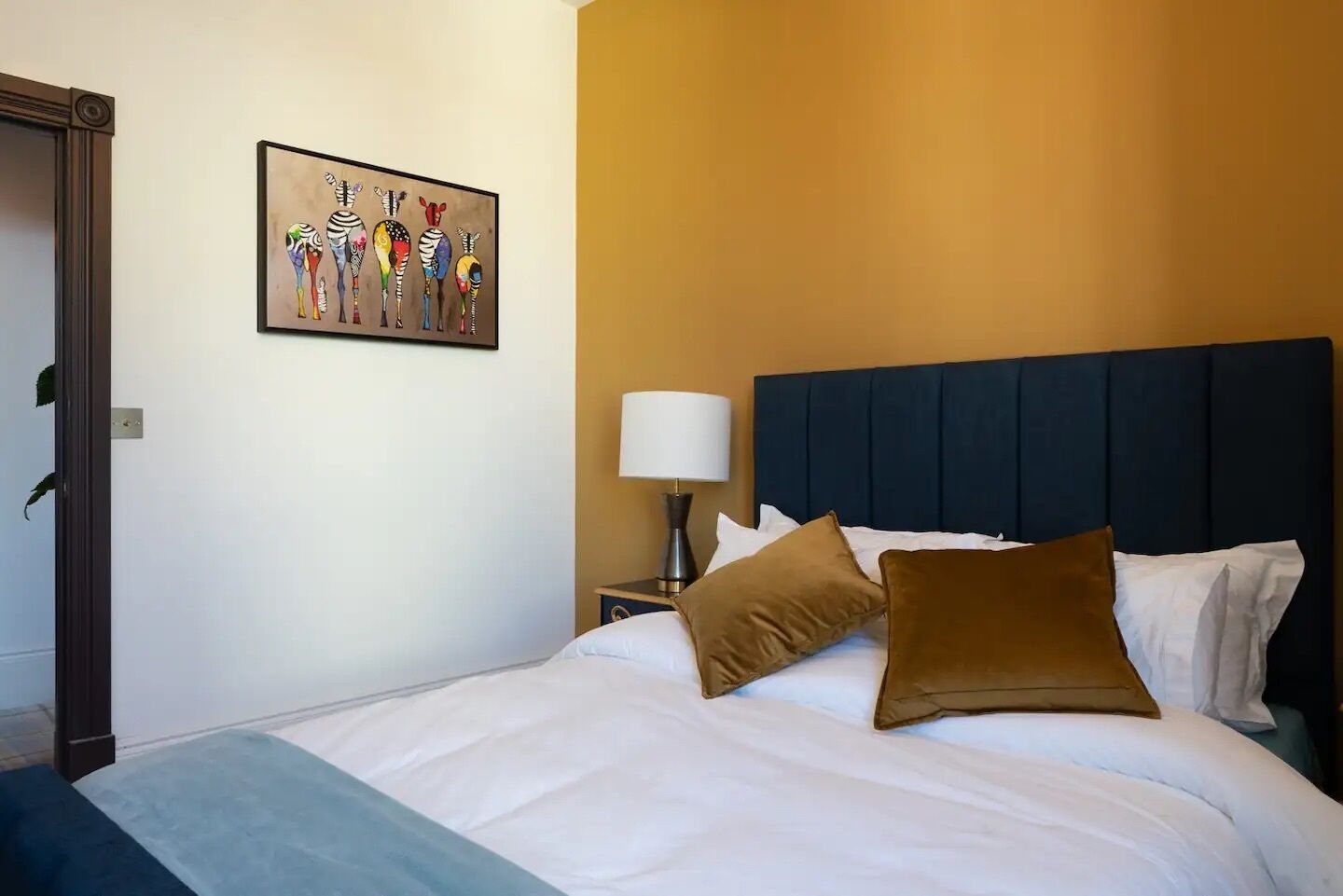 A hotel room with a bed, a nightstand, a lamp, and a colorful zebra painting on the wall.