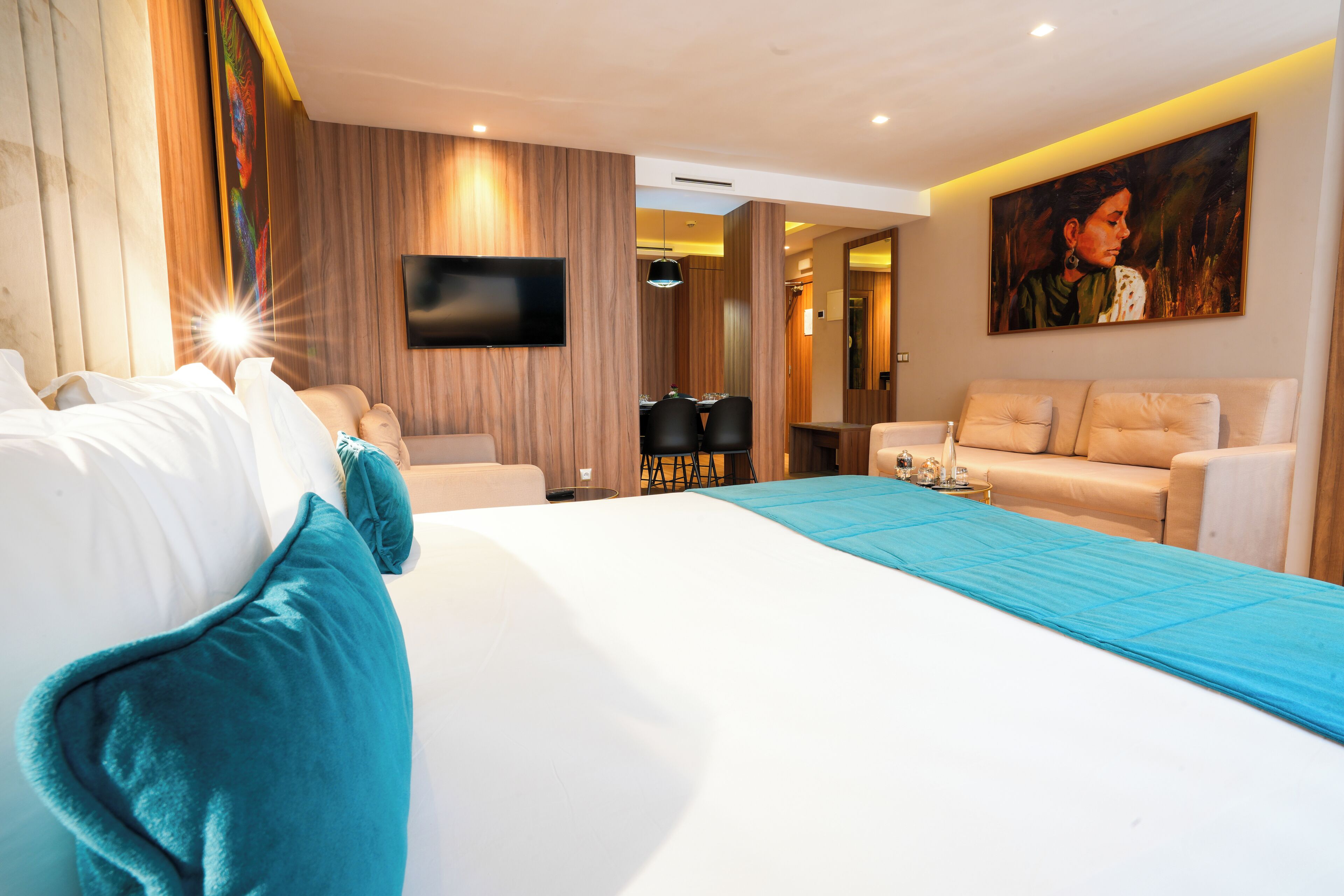 A modern hotel room with a large bed, a sofa, a TV, and a painting on the wall.