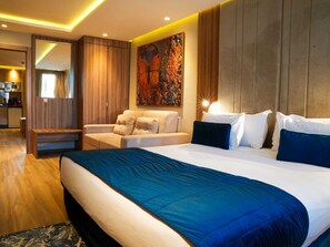 A modern hotel room with a large bed, a sofa, a desk, and a dining area visible through an open door. - First Suites Hôtel  (Rabat)