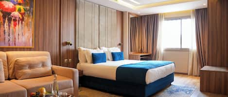 Una habitación de hotel moderna con una cama grande, un sofá, una mesita con una bandeja y un cuadro en la pared.