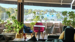 A modern outdoor seating area with multiple chairs and tables, surrounded by potted plants, and offering a view of a cityscape.