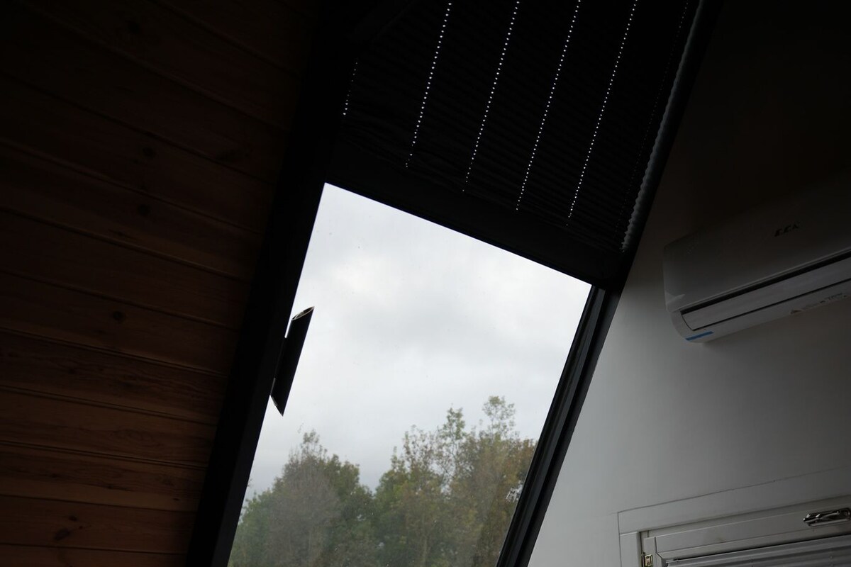 A bedroom with a large skylight, a bed, a bedside table, and an air conditioning unit.