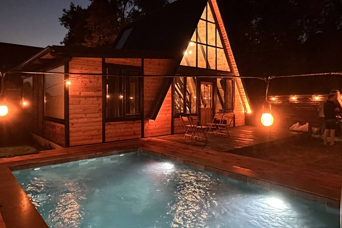 Uma cabana de madeira com telhado triangular e piscina.